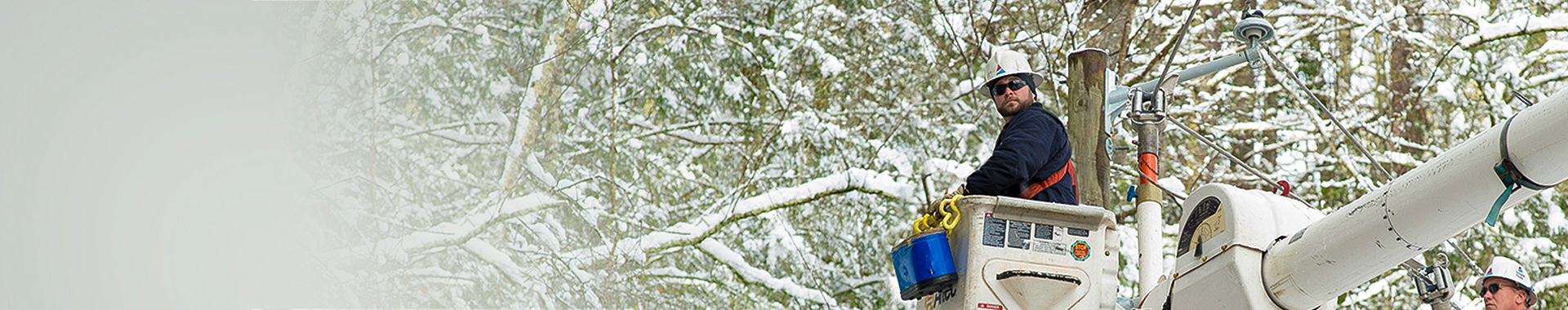 Lineworker in bucket truck near snow-covered trees