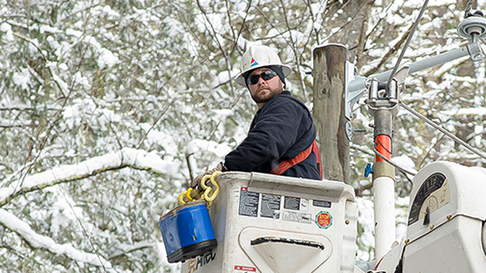 Lineworker in bucket truck near snow-covered trees